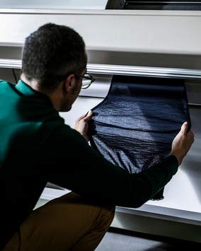 A person examining a dark knitted fabric in the atelier